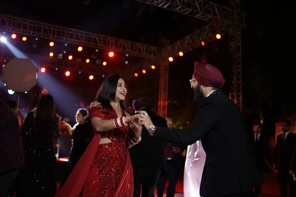 A lively moment at an Indian wedding with a couple dancing energetically amidst guests under glowing lights.