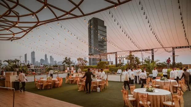 Elegant rooftop event with tables and lights set against Mumbai skyline at sunset, India.